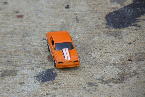 Orange hotwheels car on pavement.