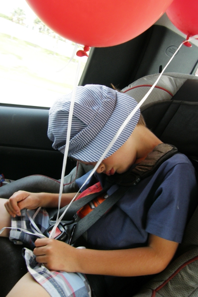 Boy with balloons, sleeping in car seat.