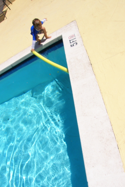 Boy picking up yellow noodle from the edge of a swimming pool.