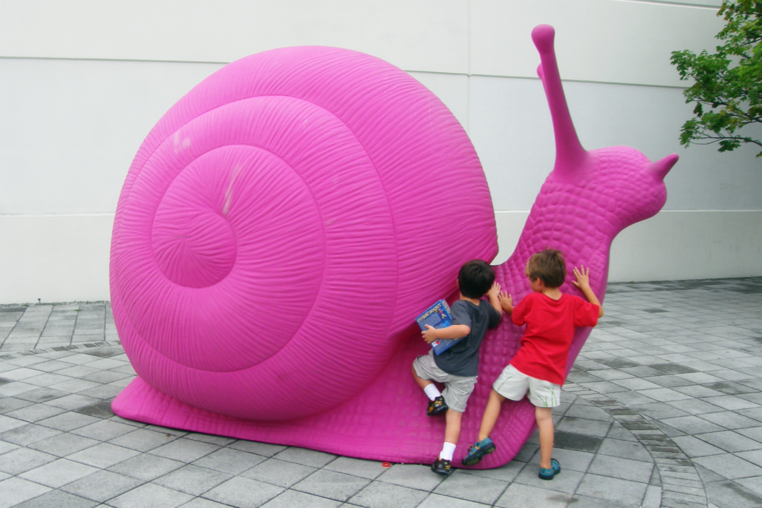 Two boys trying to climb up a sculpture of a snail