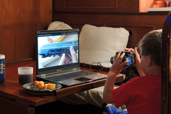 Boy taking pictures of model train video on laptop.