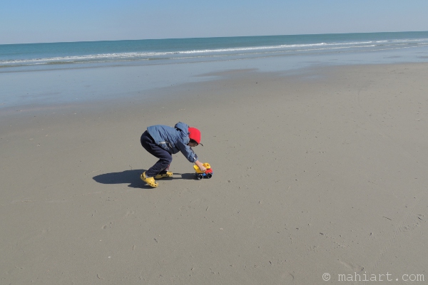 Boy pushing toy truck on the beach.