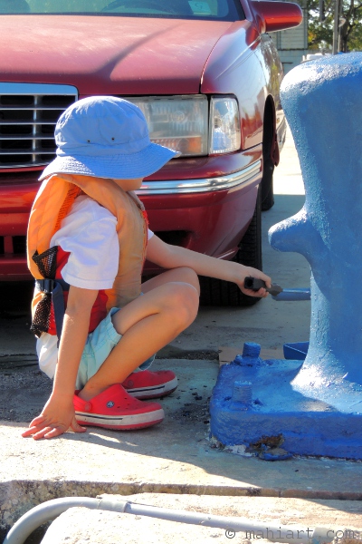 Child in blue hat painting a bollard blue