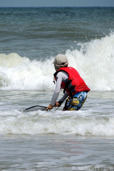 Boy in lifevest with small net fishing in the surf on the beach in South Carolina