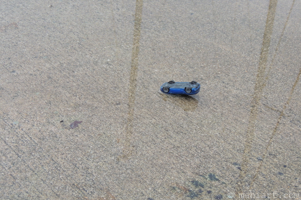 Blue toy car upside down in a rain puddle