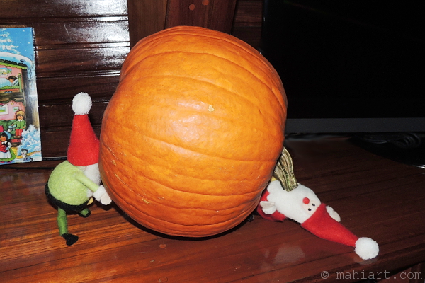 One elf rolling a pumpkin as another is getting pinned underneath