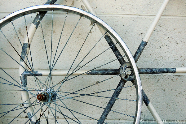 Weathered bicycle wheel and boat helm leaning against wall